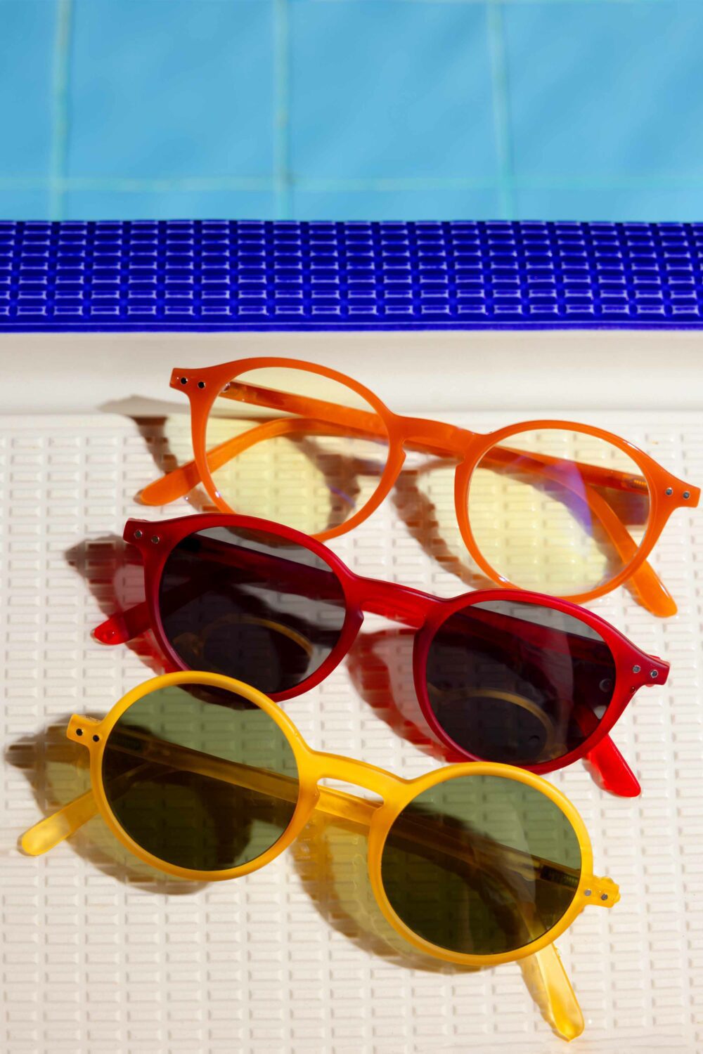 Trois paires de lunettes de soleil coloré posé aux bords d'une piscine